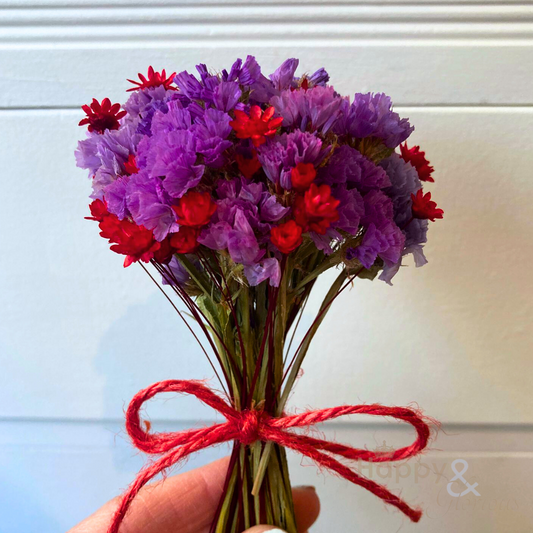 A small bunch of hand-tied dried flowers in purple and red, tied with red jute string.