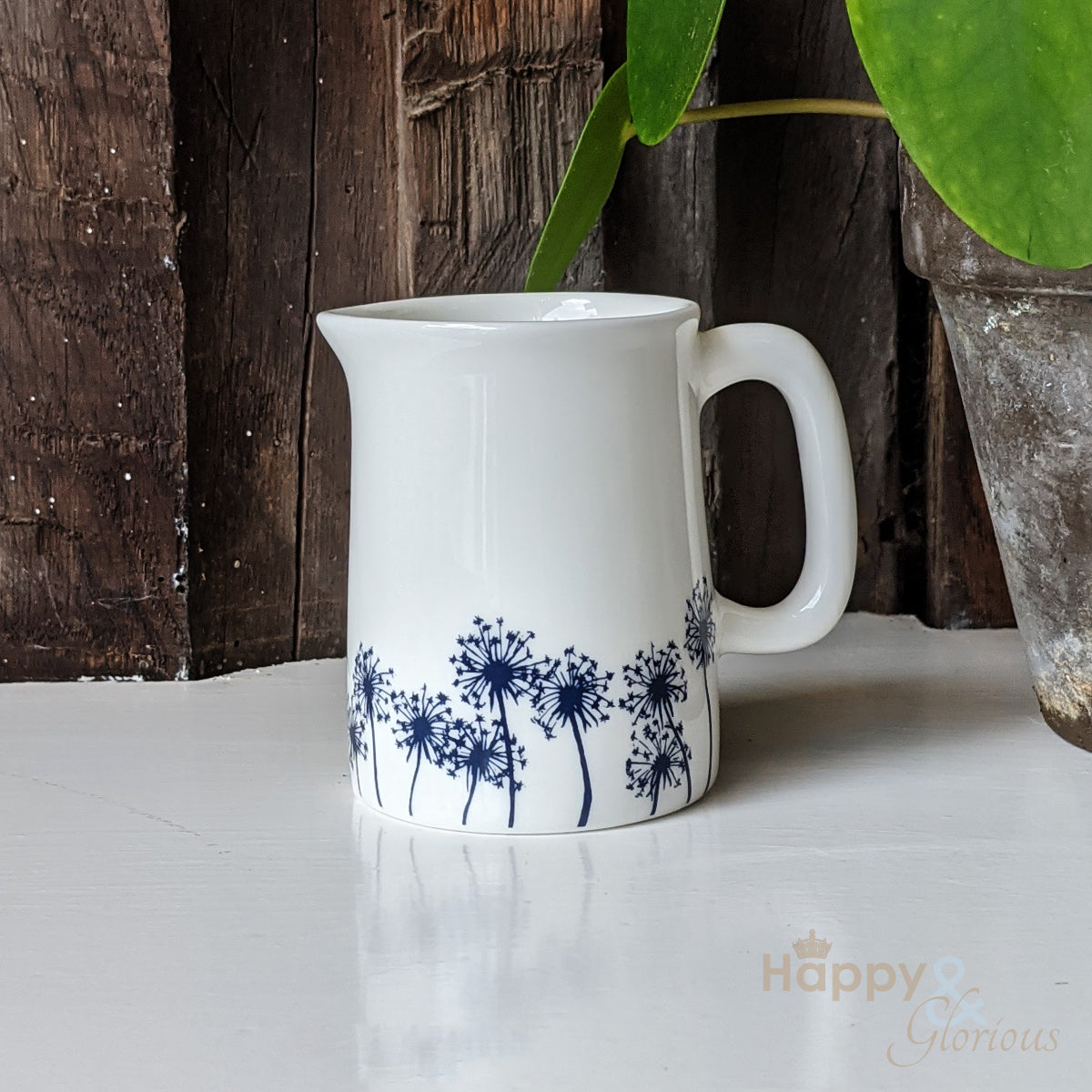 A fine bone china mini jug with navy blue silhouetted dandelion seed heads on a white background, designed by Kate Tompsett.