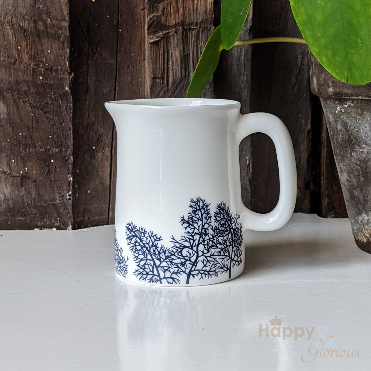 A navy blue and white fine bone china mini jug with a fennel leaf pattern, designed by Kate Tompsett, placed on a white surface with a wooden object in the background.