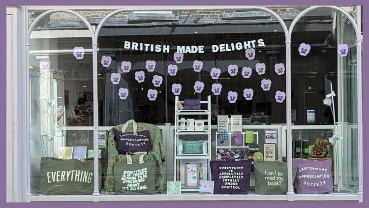 Shop windoww in Canterbury with pink black and white gifts and a display of pink bullfinches