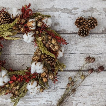 Decorative arrangement of dried flowers, cotton, and pine cones on a wooden surface