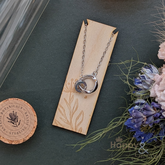 Silver necklace on a wooden card with floral elements on a dark surface