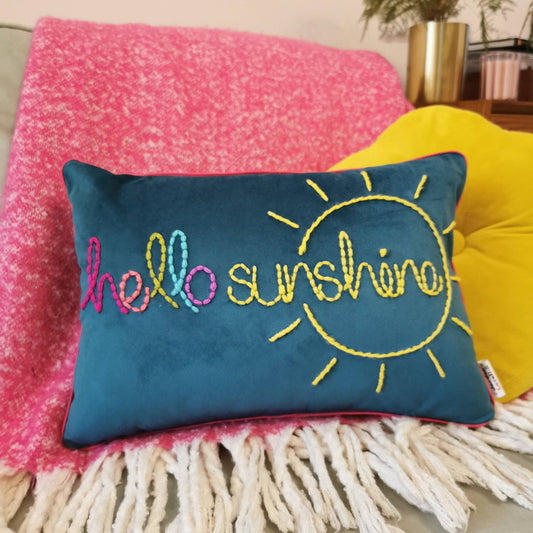 Teal pillow with 'hello sunshine' embroidery on a pink blanket