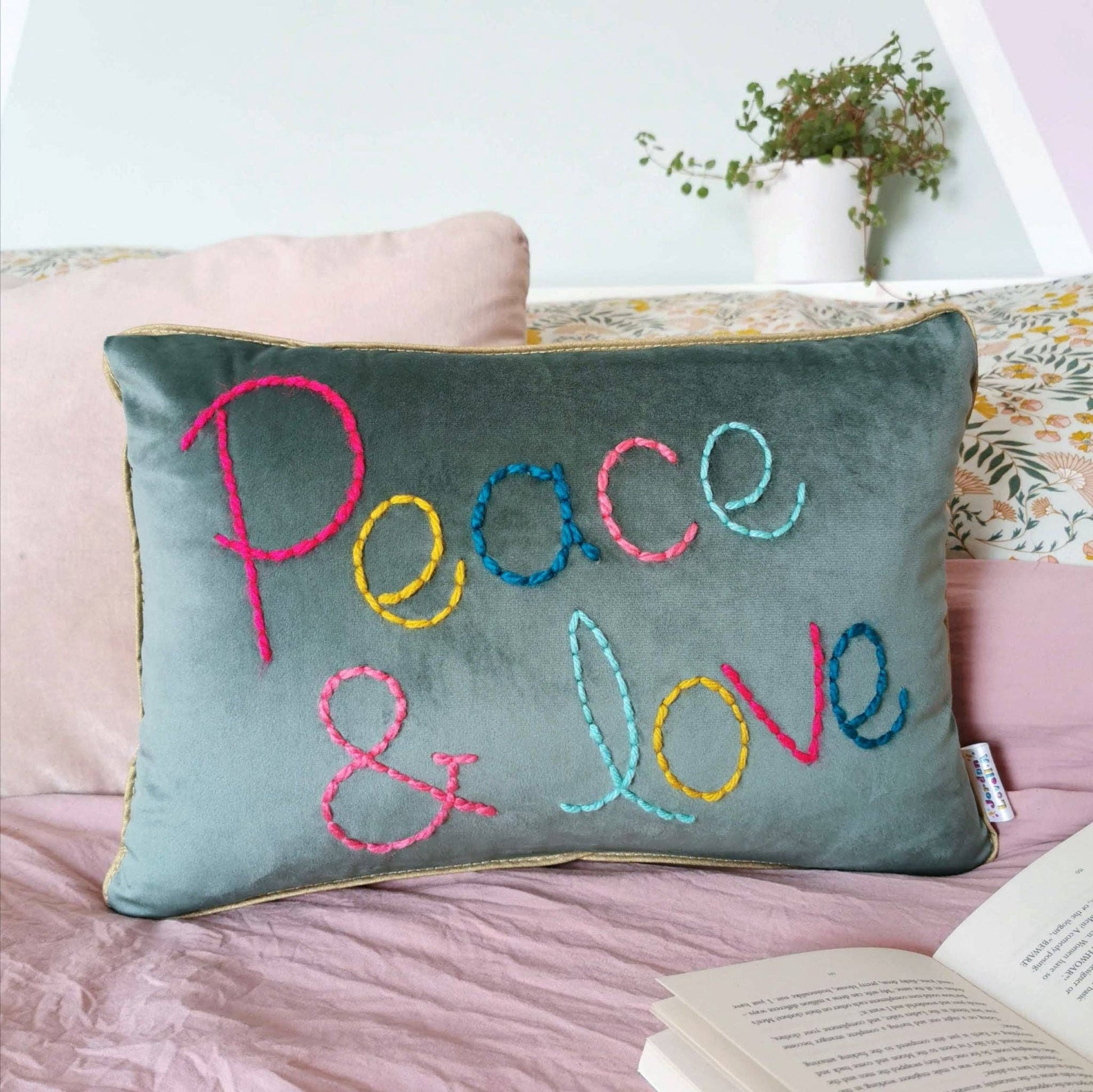 teal pillow with colorful 'Peace & Love' embroidery on a pink couch.